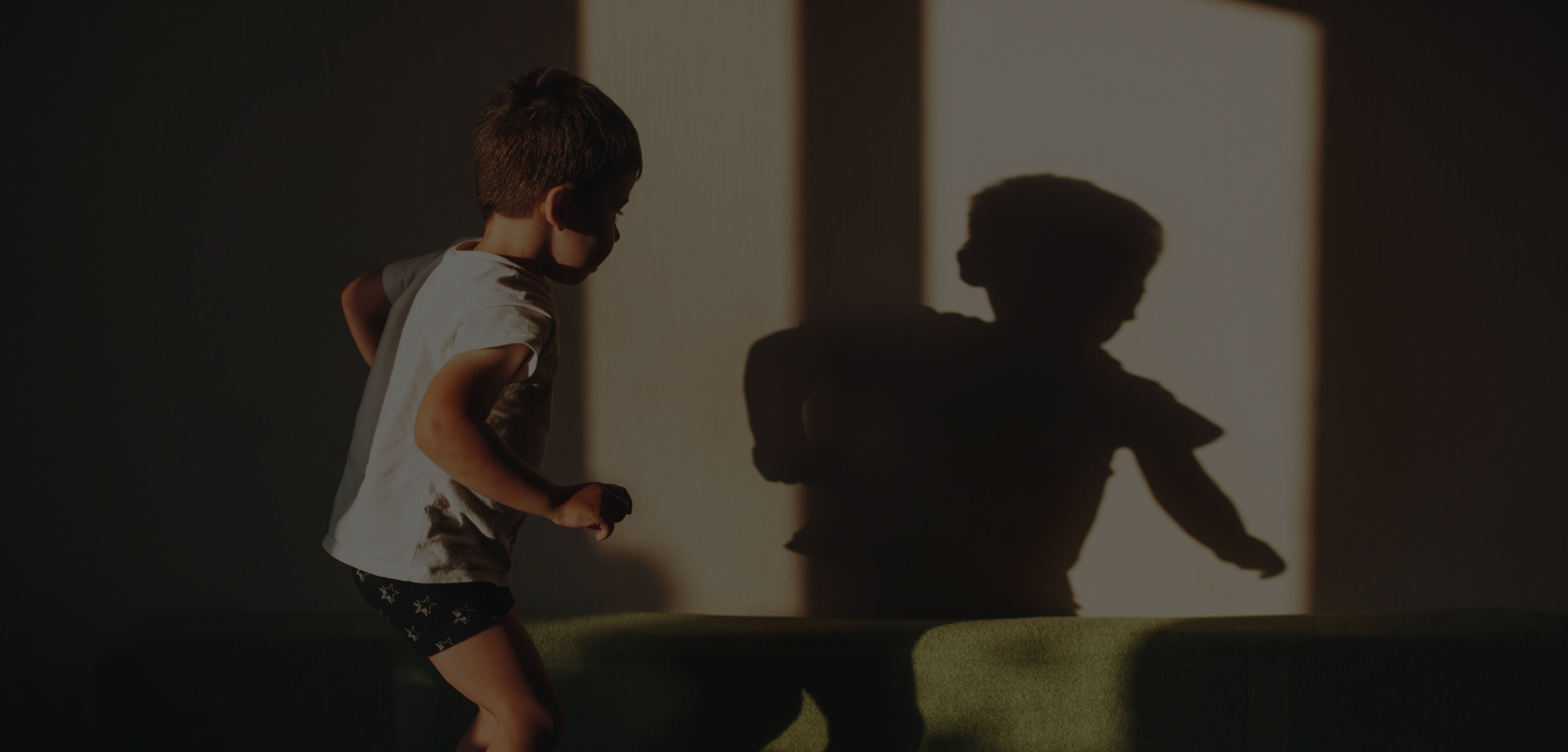 Young boy in white t-shirt and shorts playing and casting shadows on the wall