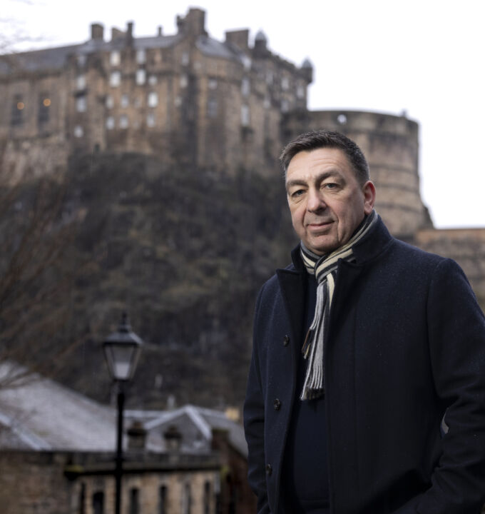 Paul stands with winter jacking and scarf on a cold morning with Edinburgh Castle in background