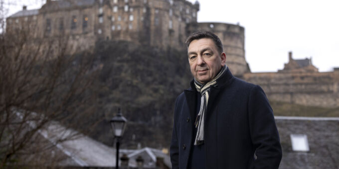 Paul stands with winter jacking and scarf on a cold morning with Edinburgh Castle in background